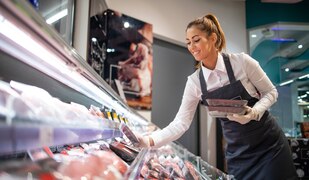 Verkäuferin an einer Kühltheke mit Fleisch