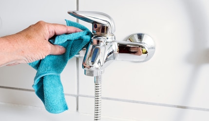 Wasserhahn wird mit Lappen von Kalk Rückständen befreit
