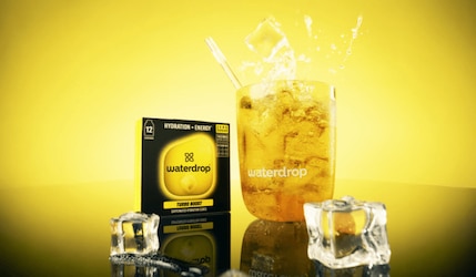 Ein Glas mit Waterdrop Turbo Boost und Eiswürfeln vor gelbem Hintergrund