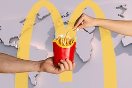 Weltkarte mit gelbem McDonald's Logo und zwei Händen die nach Pommes greifen