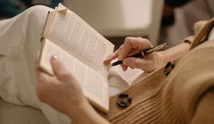 Person liest Buch und hält einen Stift