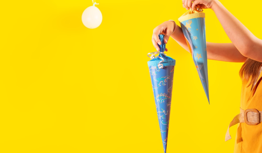 gelber Hintergrund, Mädchen hält zwei blaue Schultüten.png