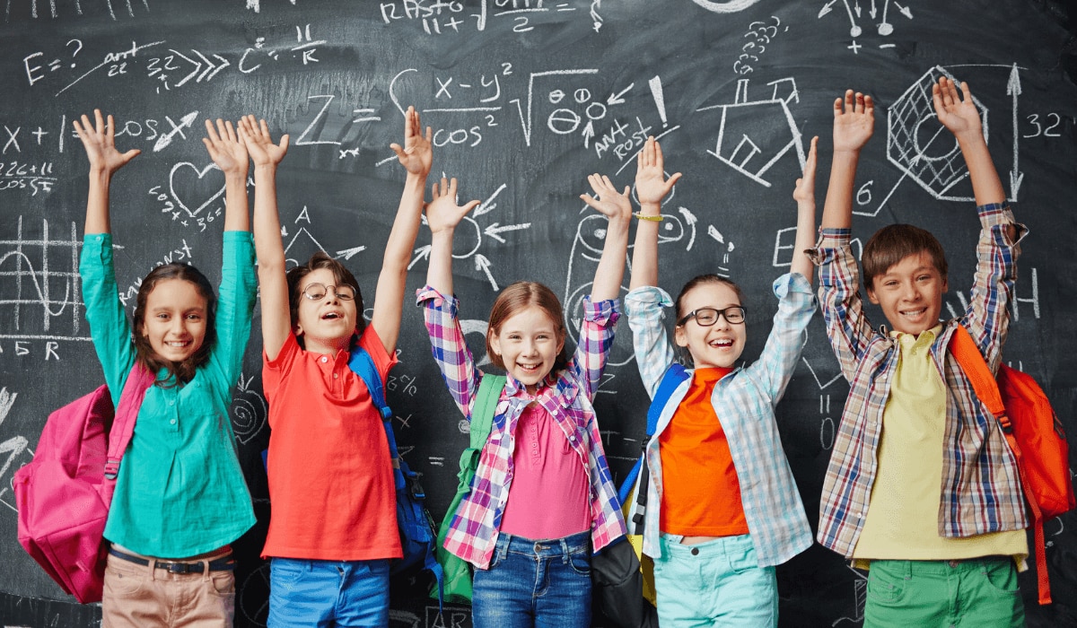 glückliche Schulkinder vor einer bemalten Schultafel