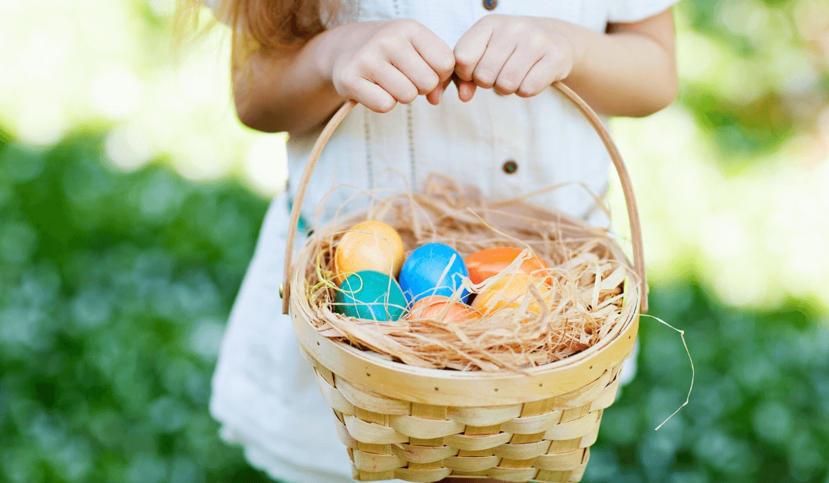 Mädchen mit Kleid hält Osterkörbchen gefüllt mit bunten Ostereiern fest