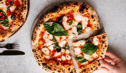 italienische Pizza aus dem Steinofen mit Besteck und einer Hand