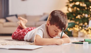 kleiner Junge schreibt mit Stiften ein Zettel an den Weihnachtsmann zu Weihnachten