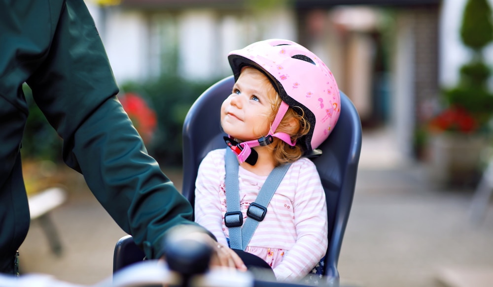 kleines Mädchen mit Helm sitzt in einem Kinderfahrradsitz