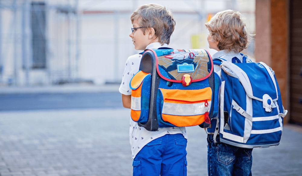 zwei kleine Jungs tragen Schulranzen auf dem Rücken, von hinten fotografiert